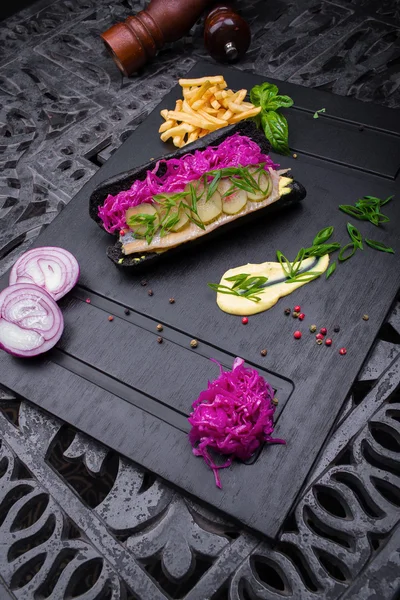 Sosisli sandviç soğan, lahana, sos ve patates kızartması bir kara tahta üzerinde siyah ekmek üzerinden