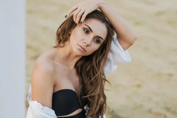 Beautiful young brunette woman in black lingerie and white shirt on the beach — Stock Photo, Image