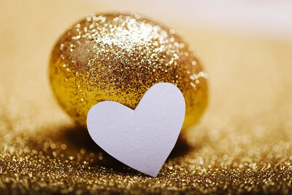 Zlatý velikonoční vajíčko s srdce n lesklé zlaté pozadí... Selektivní pozornost, mělké hloubky ostrosti — Stock fotografie