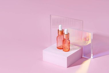 Kozmetik yağı ya da damlatıcı şişedeki serum, podyumda, pembe arka planda parlak camlarla. Sunum için şık bir zemin. Asgari düzeyde. Güzellik, kişisel bakım konsepti için kozmetik