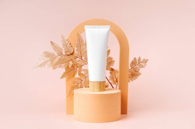 Podyumda yaprak ve kemerli krem tüp modeli. Markalaşma ve paketleme sunumu için bej rengi arkaplan. Doğal cilt bakım ürünü konsepti.