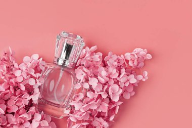 Pastel arka planda pembe çiçekli parfüm şişesi. Güzellik konsepti