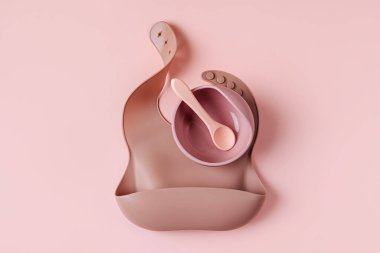 Çocuk kasesi, kaşık ve silikon önlük seti. Pembe ve kahverengi yemek takımı. Beslenme ve beslenme konsepti. Üst manzara, düz uzanma