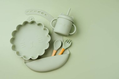 Yeşil silikon bebek önlüğü, tabak ve bardak. Bebeğe servis yapıyorum. Akşam yemeği için ilk bebek aksesuarları. Üst manzara, düz uzanma