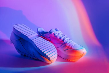 Canlı soyut arka planda moda spor ayakkabıları. Neon ışıklı spor ayakkabılar. Mor ve turuncu gradyan.  