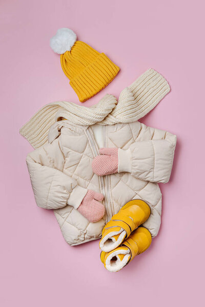 Kids warm puffer jacket with yellow  hat and boots on pink background. Stylish childrens outerwear. Winter fashion outfit 