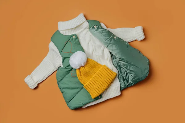 Green vest jackets with warm sweater on orange background. Stylish childrens outerwear. Winter fashion outfit
