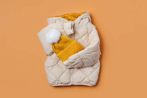 Kids warm puffer jacket with yellow  hat on orange background. Stylish childrens outerwear. Winter fashion outfit 