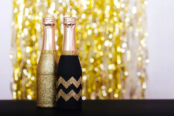 Decorative sparkly champagne bottles with serpentine on light background — Stock Photo, Image