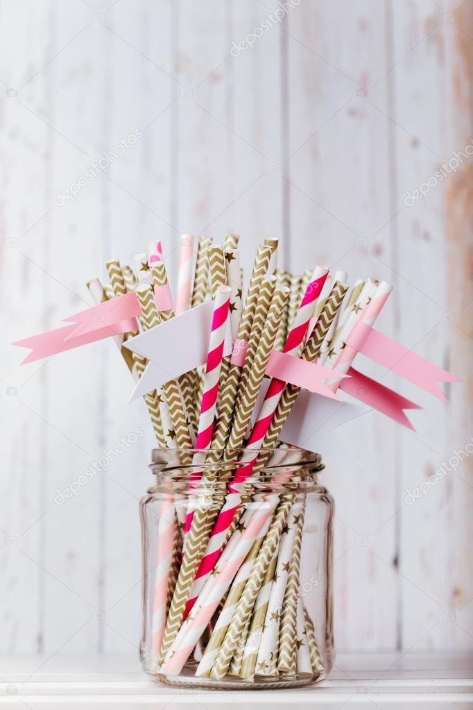 Striped mixed gold and pink drink straws in a glass jar with a sticker on a light wood background