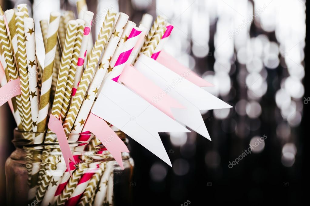 Striped mixed gold and pink drink straws in a jar with a sticker on blurred background with black shiny bokeh