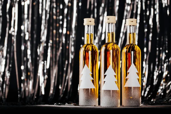 Новогодний бар. Украшенная бутылка с елкой на размытом фоне с черным блестящим боке — стоковое фото