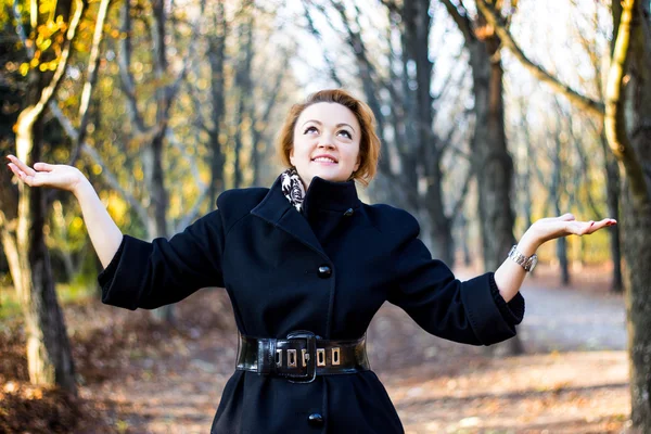 Happy young woman raising hands in autumn park