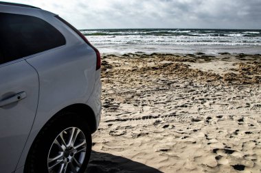 Danimarka 'nın Romo adasında deniz kenarında güzel bir plaja park edilmiş beyaz bir araba.