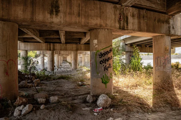 Türkiye 'nin Kemer kentinde kurumuş çimenler, yeşil bitkiler ve kumlu toprakla kirli beton bir yol köprüsü altında