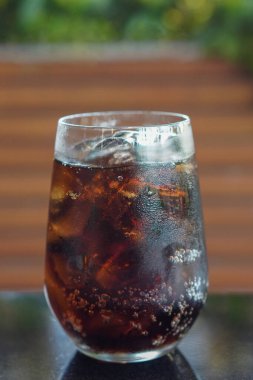 Yakın plan soğuk siyah içecek, buz, temiz bir bardakta, siyah mermer bir masaya yerleştirilmiş, kahverengi ahşap duvar arka planı, içecek, serin, taze, nesne, kopyalama alanı