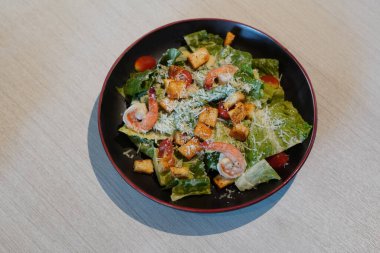 Karides, kızarmış ekmek, domates ve yeşil sebzeli salata. Ahşap zemin üzerinde siyah ve kırmızı bir tabakta.