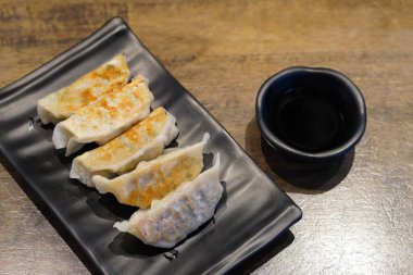 Siyah seramik tabakta beş parça gyoza ve siyah seramik bardakta sos. Ahşap zemin zemin, yiyecek, atıştırmalık, kopyalama alanı.