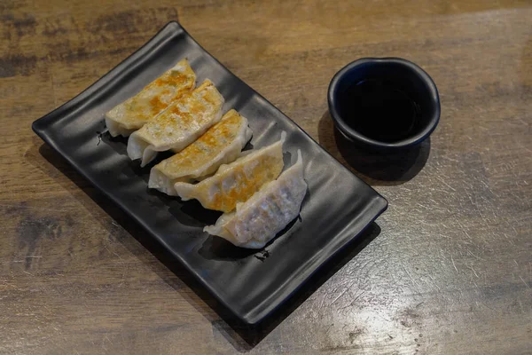 En üstteki beş gyoza siyah seramik tabakta ve siyah seramik bardakta sos ahşap zemin zemin zemininde, yemek, çerez, dekor, moda, kopyalama alanı