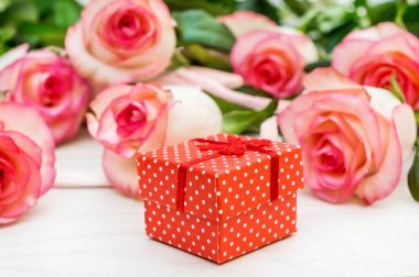 Beyaz masanın üzerinde bir buket gül olan hediye kutusu..