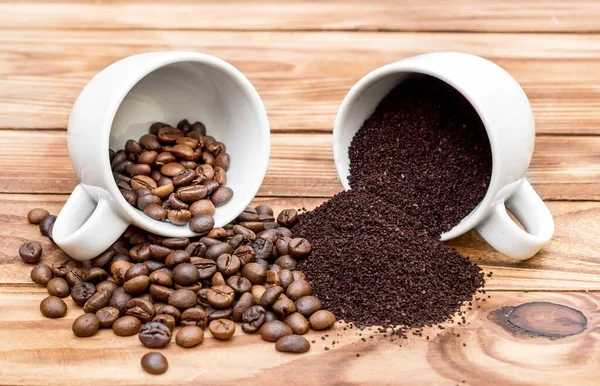 Coffee beans with ground coffee scattered from cups on the wooden table.