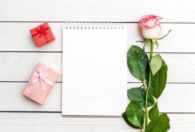 İçinde güzel bir gül ve beyaz ahşap masa üzerinde hediye kutuları olan boş bir not defteri. Üst Manzara. Metin için boşluk.