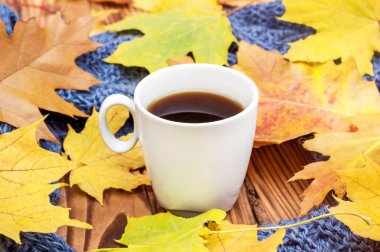 Sonbahar yapraklı bir fincan kahve ve ahşap arka planda örülmüş eşarp.. 