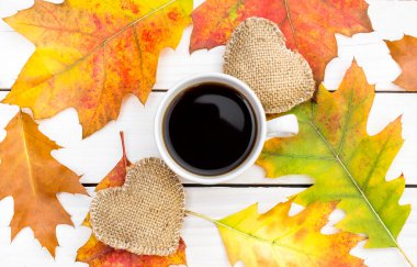 İki çuval kalpli bir fincan kahve ve beyaz ahşap masada sonbahar yaprakları