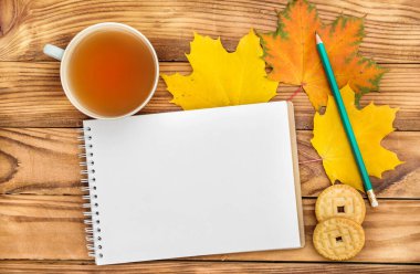 Masada sonbahar yapraklı çay ve kurabiye dolu boş bir not defteri. Metin için boşluk.