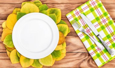 Çatal, bıçak ve sonbahar yapraklarıyla dolu boş bir tabak. Üst görünüm.