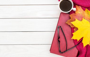 Kapalı bir kitap, bir fincan kahve, örgü eşarp ve beyaz ahşap masada sonbahar yaprakları. Üst Manzara. Metin için boşluk.