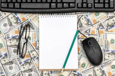 Dolar banknotlarının arka planında gözlüklü, bilgisayar faresi ve klavyeli boş not defteri.