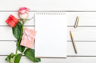 İçinde güzel bir gül ve beyaz ahşap masa üzerinde hediye kutuları olan boş bir not defteri. Üst Manzara. Metin için boşluk.