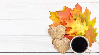 İki çuval kalpli bir fincan kahve ve beyaz ahşap masada sonbahar yaprakları