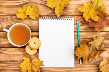 Masada sonbahar yapraklı çay ve kurabiye dolu boş bir not defteri. Metin için boşluk.