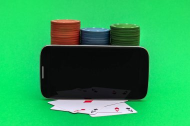 Boş ekranlı akıllı telefon, poker fişleri ve yeşil arka planda iskambil kartları. Çevrimiçi poker. Metin için boşluk.