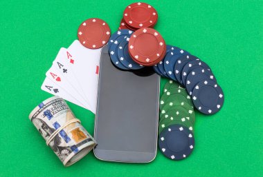Boş ekranlı akıllı telefon, poker fişleri, yeşil arka planda iskambil kartları ve para. Üst görünüm.