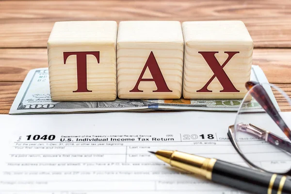 Word tax with tax form, money and glasses on the desk.