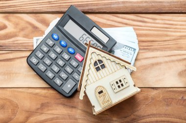 Hesap makinesi ve masada para olan bir ev modeli. Üst görünüm.