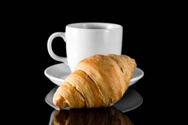 Bir fincan kahve ve kruvasan siyah yansıtıcı arka plan..