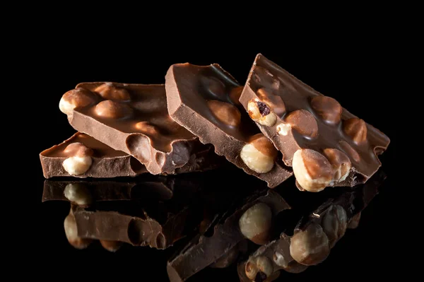 Stukken Gebroken Chocoladereep Met Hele Noten Zwarte Reflecterende Achtergrond — Stockfoto