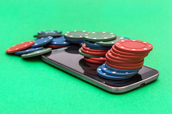 Smartphone with poker chips on green background. 