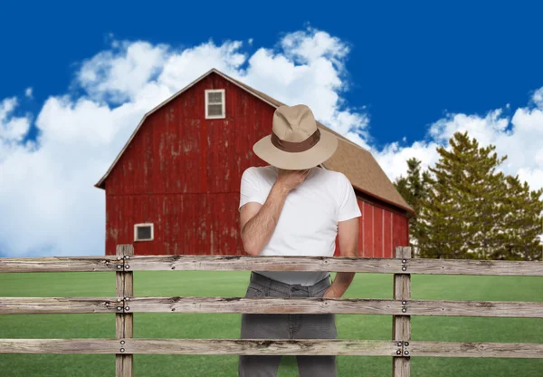 sad farmer wearing a hat behind the fence