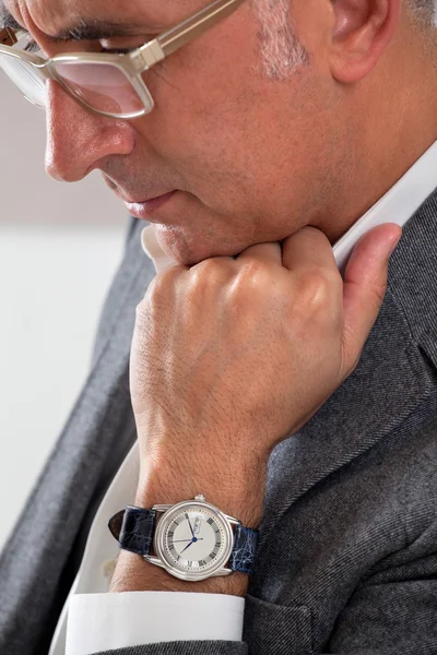 Hombre mostrando su reloj mientras piensa con la mano en la barbilla mirando hacia abajo — Foto de Stock