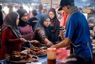 Langkawi, Malezya - Haziran 2019: Asyalı kadınlar sokak pazarından yiyecek seçerler. Kimliği belirlenemeyen Asyalılar gece marketi yürüyüş caddesinde yemek satıyorlar. Geleneksel Asya sokak pazarı.