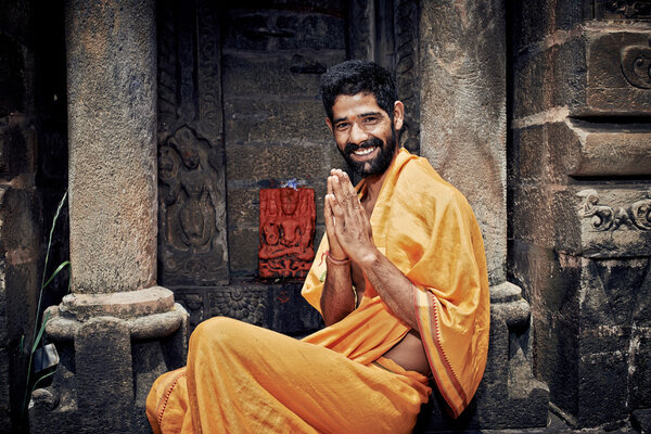 Smiling Indian Brahmin. sitting near the temple of Lord Krishna. Hands folded in namaste mudra.