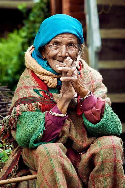 Evini avluda oturan eski kırsal Hintli kadın. Kameraya gülümseyen.