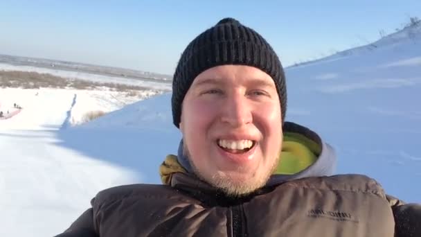 Porträt eines jungen Mannes, der im Winter den Berg hinunterkommt, lächelt und in die Kamera blickt . — Stockvideo