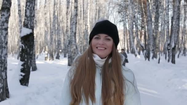 Primer plano de una chica bonita sonriendo en movimiento, mirando a la cámara en el bosque de invierno. Fondo desenfocado en bosque de invierno — Vídeos de Stock