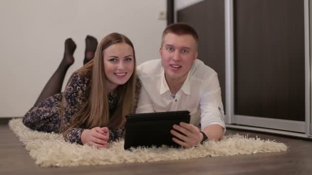 Portrait of a happy European young couple lying on lounge floor using Digital Tablet — Stock Video